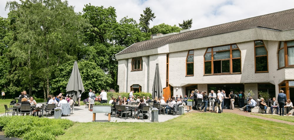 Een zonnig terras gevuld met gasten naast het witte gebouw van Antropia
